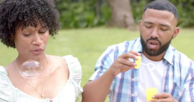 Mutlu Afro-Amerikan çifti bahçede oturmuş baloncuk üflüyor, ağır çekimde. Eğlence, boş zaman, birliktelik ve yaşam tarzı, değişmemiş..