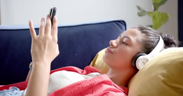 Happy Biracial Teenage Girl Headphones Lying Couch Using Smartphone Smiling — Stock Video