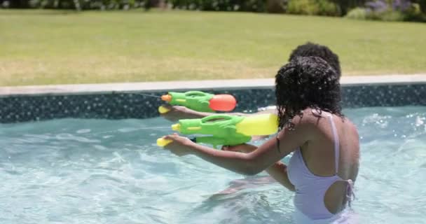 ハッピーアフリカ系アメリカ人の両親と娘は 晴れたプールでウォーターピストルで遊んでいます 楽しみ 相互関係 自由な時間 リラクゼーションおよびライフスタイル 変わらない — ストック動画
