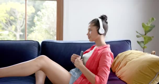Feliz Chica Adolescente Birracial Auriculares Tumbados Sofá Con Teléfono Inteligente — Vídeos de Stock
