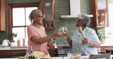 Mutlu son sınıf Afro-Amerikan bayan arkadaşları yavaş çekimde yemek pişirirken şarapla kadeh kaldırıyor. İletişim, içki, yemek, yemek, arkadaşlık, refah ve sağlıklı yaşlı yaşam tarzı, değişmemiş.