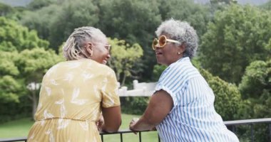 Güneş gözlüklü yaşlı Afro-Amerikan bayan arkadaşlarının portresi balkonda gülüyor, ağır çekimde. Yaz, eğlence, tatiller, rahatlama, arkadaşlık, birliktelik ve son sınıf yaşam tarzı, değişmemiş..