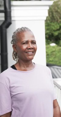 Bahçede gülümseyen yaşlı Afrikalı Amerikalı kadının dikey video portresi, yavaş çekim. Refah ve sağlıklı yaşlı yaşam tarzı, değişmedi..