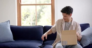 Karton kutuda teslimat yapan mutlu çift ırklı adam akıllı telefon, kopyalama alanı ve ağır çekim kullanıyor. İletişim, dağıtım, paket, kargo, çevrimiçi alışveriş, ev hayatı ve yaşam tarzı, değiştirilmemiş.