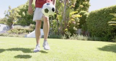 Güneşli bahçede, fotokopi alanında, ağır çekimde, çift ırklı bir adamın futbolla pratik yapma becerisinin düşük kesimi. Futbol, beceri, eğitim, yaz, antrenman, spor, spor ve sağlıklı yaşam tarzı, değişmemiş.