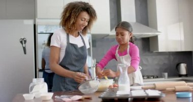 Mutlu çift ırklı anne ve kız kek karışımı yapıyor, mutfakta pişiriyor, yavaş çekimde. Annelik, çocukluk, birliktelik, yemek, yemek pişirme, pişirme, ev hayatı ve yaşam tarzı, değişmemiş.