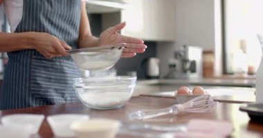 Çift ırklı mutlu kadın önlüklü, un süzen, mutfakta pişiren, ağır çekimde. Yemek, yemek pişirme, ev hayatı ve yaşam tarzı, değişmemiş..