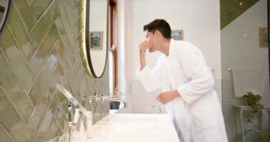 Banyodaki aynada saçı ve yüzü inceleyen çift ırklı bir adam, kopyalama alanı, yavaş çekim. Kişisel bakım, refah, ev hayatı ve yaşam tarzı, değişmemiş..