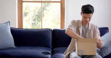 Karton kutuda teslimat yapan mutlu çift ırklı adam akıllı telefon, kopyalama alanı ve ağır çekim kullanıyor. İletişim, dağıtım, çevrimiçi alışveriş, kargo, paket, ev hayatı ve yaşam tarzı, değiştirilmemiş.