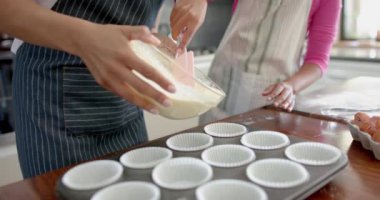 Melez anne ve kızının pasta karışımlarını mutfakta yavaş çekimde pasta formlarına koymasının orta kısmı. Annelik, çocukluk, birliktelik, yemek, yemek pişirme, pişirme, ev hayatı ve yaşam tarzı, değişmemiş.