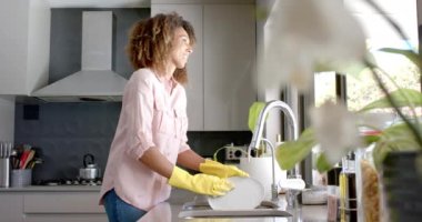 Güneşli mutfakta bulaşık yıkayan mutlu çift ırklı kadın fotokopi alanı, ağır çekim. Temizlik, angarya, hijyen, ev hayatı ve yaşam tarzı, değişmemiş..