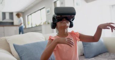 Oturma odasında sanal arayüz kullanarak VR kulaklık takan mutlu çift ırklı kız, yavaş çekim. Çocukluk, keşif, teknoloji, dijital arayüz ve ev hayatı, değiştirilmemiş.