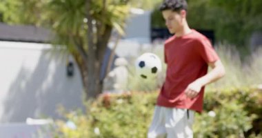 Güneşli bahçede, fotokopi alanında, ağır çekimde futbol oynayan çift ırklı bir adam. Futbol, beceri, eğitim, yaz, antrenman, spor, spor ve sağlıklı yaşam tarzı, değişmemiş.