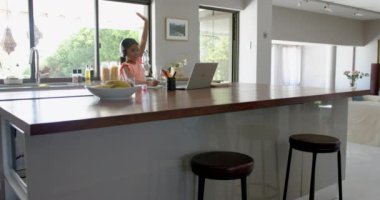 Melez kız, ilkokulda dizüstü bilgisayarda, mutfakta el kaldırıyor, ağır çekimde. Eğitim, iletişim, okul, öğrenme, çocukluk, teknoloji ve ev hayatı, değiştirilmemiş.