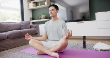 Yoga meditasyonu ve nefes alma pratiği yapan çift ırklı bir adam yerde oturuyor, kopyalama alanı, yavaş çekim. Yoga, meditasyon, derin nefes alma, fitness, refah, ev hayatı ve sağlıklı yaşam tarzı, değişmemiş.