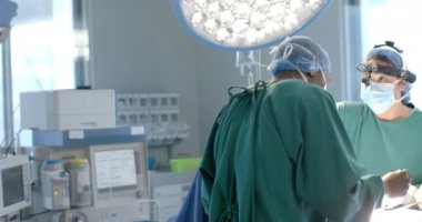 Maskeli çeşitli kadın ve erkek cerrahlar operasyon sırasında ekipmanları kontrol ediyor, ağır çekim. Takım çalışması, operasyon, ameliyat, hijyen, tıbbi ekipman, hastane, tıp ve sağlık hizmetleri, değiştirilmemiş.