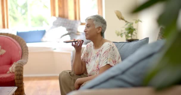 快乐的老女人坐在沙发上 在家里用智能手机聊天 动作缓慢 家庭生活 退休和生活方式 — 图库视频影像