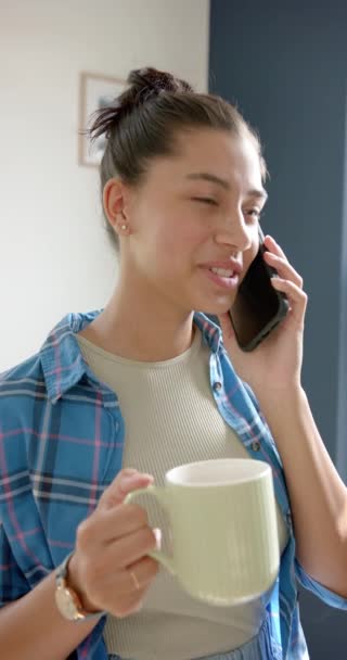 スマートフォンで話すお茶と笑顔の十代の少女の垂直ビデオ スローモーション コミュニケーション 思春期 リラックス 家庭生活 ライフスタイル — ストック動画