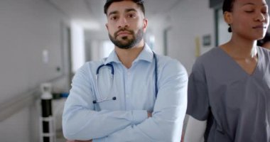 Hastane koridorunda duran tıbbi giysili kendinden emin genç Asyalı doktor. Mesleki duruşu hastalara yavaş çekimde yardım etmeye kendini adadığını ve hazır olduğunu gösteriyor..