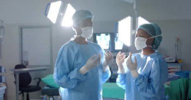 Cerrahlar parlak bir ameliyathanede ameliyata hazırlanıyorlar. Odaklanmış ifadeleri ve steril giysileri çalışmalarının ağırlığının altını çiziyor, ağır çekim..
