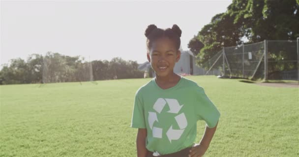 明るい女の子は緑のリサイクルTシャツを着た晴れた屋外公園に誇らしげに立っています 彼女はシャツの明るいシンボルでリサイクル意識を促進し ゆっくりとした動き — ストック動画