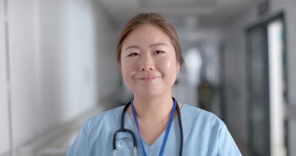 アジアの若い看護師は 病院の廊下に自信を持って立っています 彼女のプロフェッショナルな服装と暖かい笑顔は 医療現場での献身とケア スローモーションを伝えます — ストック動画