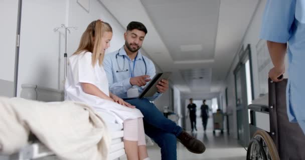 年轻的白人女孩在医院里与医生会诊 有复制空间 他们在繁忙的走廊 慢动作的平板电脑上查看医疗信息 — 图库视频影像