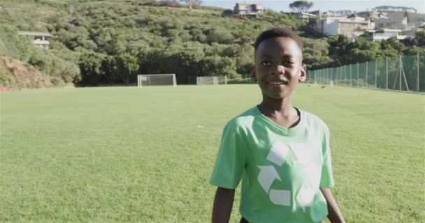 Afroamerykanin Noszący Zieloną Koszulkę Recyklingu Stoi Słonecznym Boisku Piłki Nożnej — Wideo stockowe