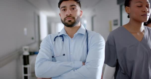 医療服を着た若いアジア人医師が病院の廊下に立っている 彼のプロのスタンスは 患者を支援するための献身と準備を伝えます 遅い動き — ストック動画