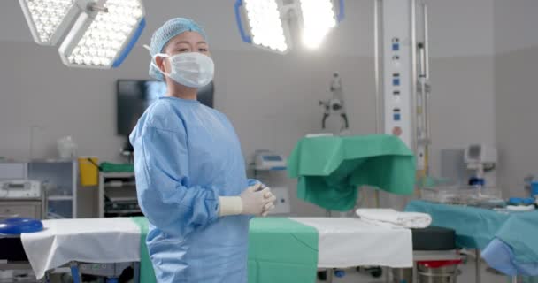 年轻的亚洲女人自信地站在一间有复印空间的医院手术室里 她的职业装束表明 她是一名医护人员 随时准备接受手术 动作缓慢 — 图库视频影像