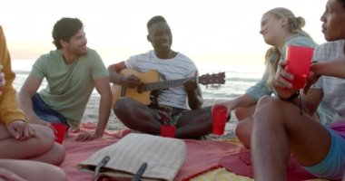 Çeşitli arkadaşlar bir partide plaj toplantısından hoşlanırlar. Genç bir Afrikalı Amerikalı gitar çalıyor, açık hava eğlence atmosferini arttırıyor, yavaş çekim..
