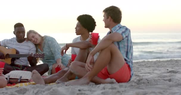 不同的朋友在日落时在海滩上欣赏音乐 一个多样化的群体在一起放松下来 创造了一个难忘的夏天时刻 慢动作 — 图库视频影像