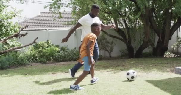 非裔美国人的父亲和儿子在户外踢足球 他们在后院里享受着阳光灿烂的一天 在运动 慢动作中彼此依偎在一起 — 图库视频影像