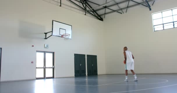 アフリカ系アメリカ人男性は コピースペースでジムでバスケットボールを練習しています 彼の焦点は 屋内コートの設定でジャンプショットを完璧にすることです スローモーション — ストック動画