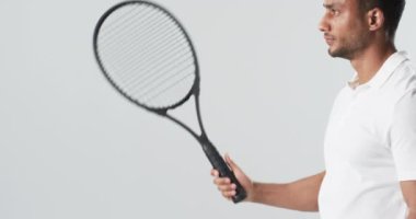Çift ırklı genç adam badminton raketiyle poz veriyor, fotokopi alanı ile. Bir stüdyo ortamında maç için özgüven ve hazırlık yayıyor, ağır çekim..