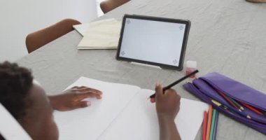 Afro-Amerikalı çocuk evde fotokopi alanı olan bir tablet kullanıyor. Okul malzemeleriyle ev ödevlerine odaklanmış, ağır çekimde..