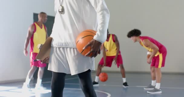 아프리카계 미국인 코치는 체육관에서 농구를 개최합니다 세션을 감독하고 플레이어에게 전략을 — 비디오