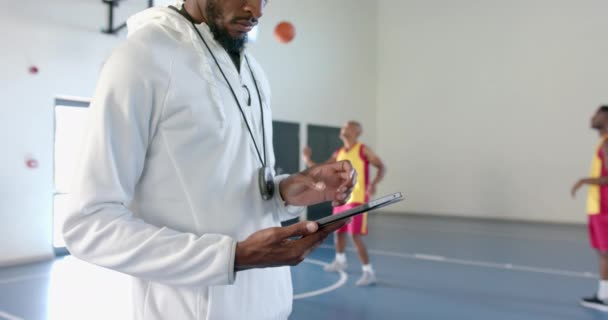 非洲裔美国人教练在一家体育设施审查平板电脑上的数据 他对运动员健康的关注从体育馆的环境 慢动作等方面都很明显 — 图库视频影像