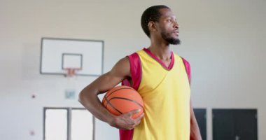 Afrikalı Amerikalı bir adam spor salonunda güven içinde poz veriyor. Atletik kıyafetleri yavaş çekimde bir basketbol maçına hazır olduğunu gösteriyor..