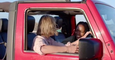 Genç Afrikalı Amerikalı kadın ve beyaz kadın bir araba yolculuğunda fotokopi uzayı ile aynı kahkahayı paylaşıyorlar. Neşeli etkileşimleri spontane bir anı vurguluyor..