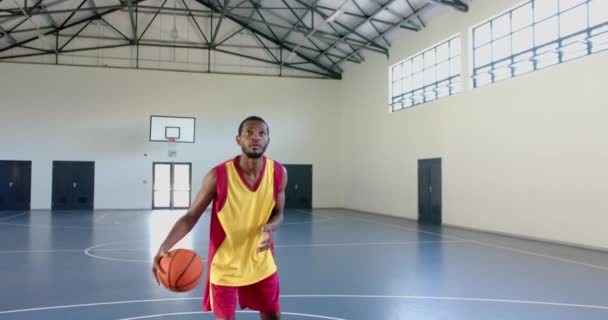 アフリカ系アメリカ人が屋内裁判所でバスケットボールを撃った 彼の焦点とフォームは スクールジムでのゲームの強度をキャプチャ スローモーション — ストック動画