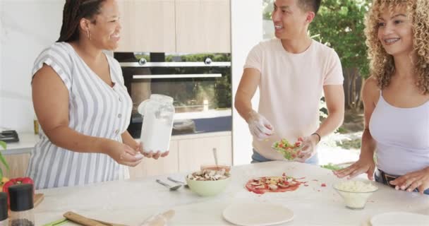 若いアジア人男性と女性は ピザを作っている間 家庭のキッチンで笑います 小麦粉や野菜は 友人の間で楽しい料理セッションを提案しています スローモーション — ストック動画