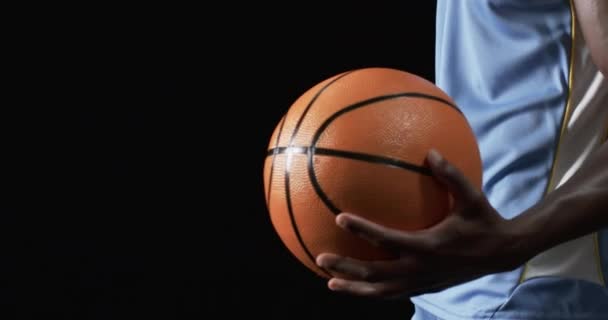 黑人男子拿着一个黑人背景的篮球 他的握力和姿势暗示他已经准备好参加一场比赛或练习 慢动作 — 图库视频影像