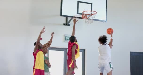 若いアフリカ系アメリカ人男性は屋内でバスケットボールを楽しんでいます 彼らのエネルギッシュなプレーは ジムの設定 スローモーションでチームワークと体力にハイライトします — ストック動画