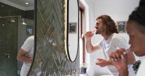 若い白人男性は 現代的なバスルームで歯を磨いています 彼らは歯科衛生 遅い動きに焦点を当て 朝のルーチンを維持しています — ストック動画