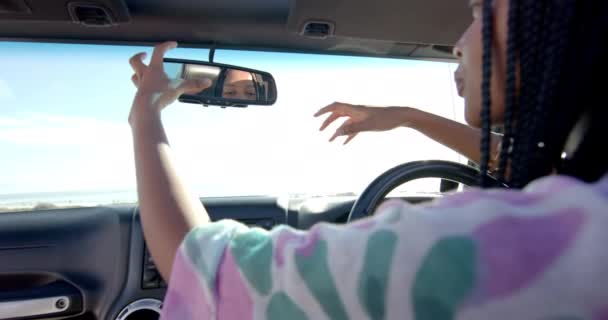 若いアフリカ系アメリカ人女性は 彼女の車の後部ビューミラーを道路旅行で調整します 彼女は運転中に集中した瞬間に捕らえられ 道路上の安全を確保し ゆっくりとした動き — ストック動画