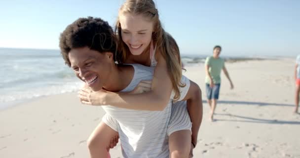 Young Caucasian Woman Enjoys Piggyback Ride African American Man Beach — Stock Video