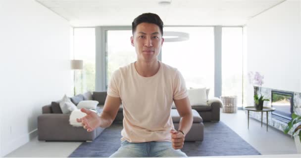 年轻的亚洲男子在一个现代客厅里随意地坐在一个视频通话 他那悠闲的姿势暗示了在家里的舒适和悠闲 动作缓慢 — 图库视频影像