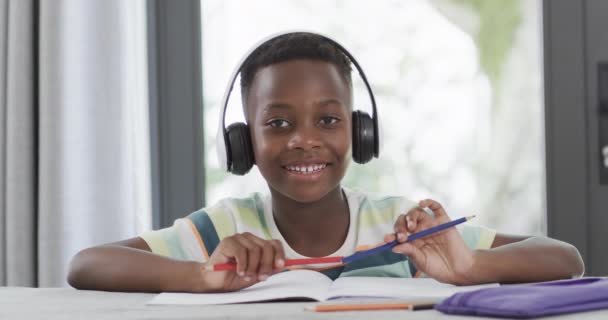 自宅でのアフリカ系アメリカ人の少年研究は ヘッドフォンを着用している間 彼の学校の仕事に焦点を当てました スローモーション — ストック動画