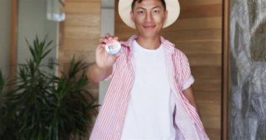 Genç Asyalı adam bir 'VOTE' rozeti gösteriyor. Gururla gülümseyerek, yurttaşların katılımını teşvik ediyor, ağır çekimde..